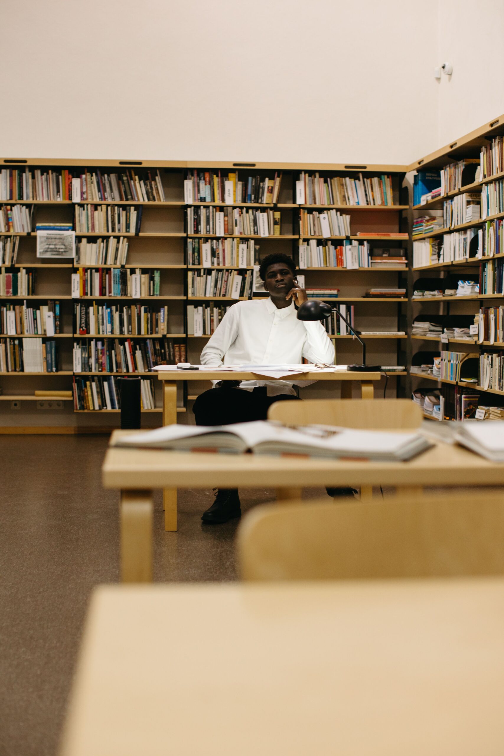 Pensive man sitting and thinking in a library surrounded by bookshelves.